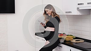 Cheerful pregnant woman with a phone in the kitchen