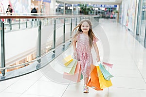 Cheerful preschool girl walking with shopping bags. Pretty smiling little girl with shopping bags posing in the shop. The concept