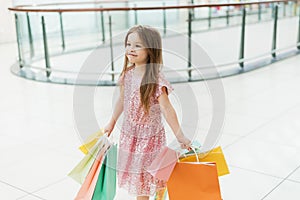 Cheerful preschool girl walking with shopping bags. Pretty smiling little girl with shopping bags posing in the shop. The concept