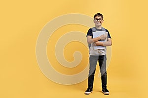 Cheerful preteen boy schooler with backpack and notebooks on yellow