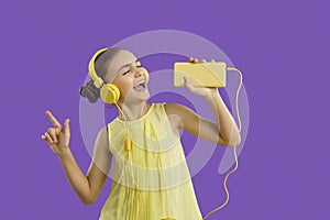 Cheerful preteen girl in headphones connected to mobile phone listens to music and sings along.