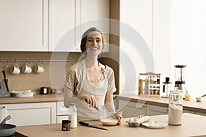 Cheerful pretty adult baker girl in apron enjoying culinary hobby