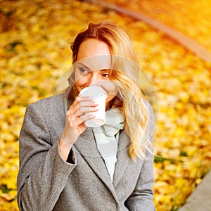 Cheerful pretty woman drinking coffee in autumn park