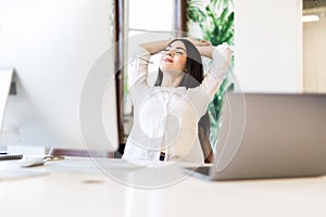 Cheerful pretty woman sitting at desk with hands behind head. Business lady imagines happy future with closed eyes. Relaxed girl