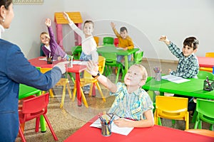 Cheerful pupils raising hands to answer