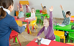 Cheerful pupils raising hands to answer