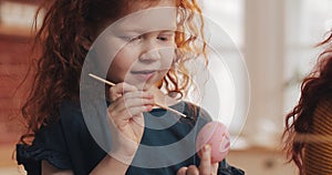 Cheerful redhead little kid girl with her mother painting easter egg on the kitchen background. Happy easter