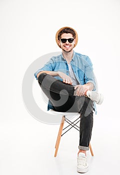 Cheerful relaxed man in hat and glasses sitting on chair