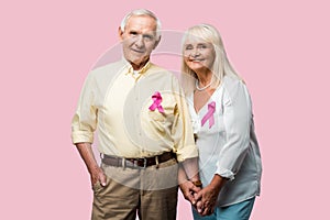 cheerful retired couple with grey hair and ribbons isolated on pink.