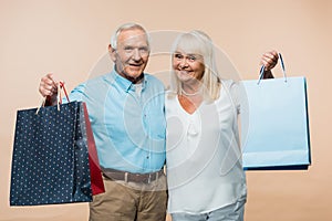 cheerful retired couple holding shopping bags and smiling isolated on beige.