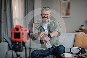 Cheerful retired european man with beard makes overview of devices and shows smart watch