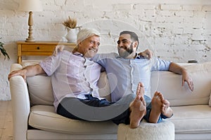 Cheerful retired father and grownup adult relaxing on comfortable couch