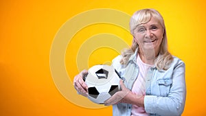 Cheerful retiree woman holding football ball, sports betting, positive attitude