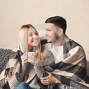 Cheerful romantic couple is sitting on sofa under cozy plaid