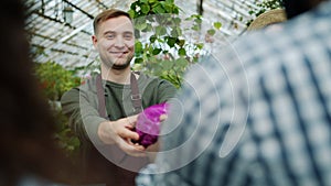 Cheerful salesman giving organic food to customer in greenhouse market