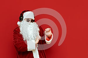 Cheerful Santa Claus in sunglasses dancing on a red background, listening to music in headphones and having fun at a party. Santa photo