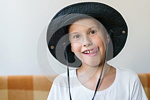 Cheerful school-age boy in white t-shirt and black hat sits on the couch