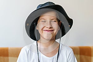 Cheerful school-age boy in white t-shirt and black hat sits on the couch