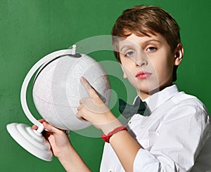 Cheerful school boy in white shirt holding globe in hands on green