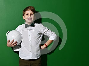 Cheerful school boy in white shirt holding globe in hands on green