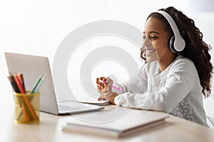 Cheerful school girl having online lesson, using laptop at home