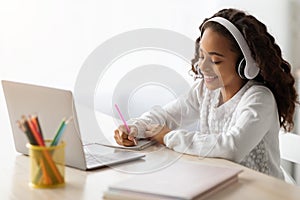 Cheerful school girl having online lesson, using laptop at home