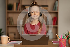 Cheerful School Girl Using Laptop Wearing Earphones At Home