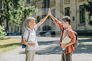 Cheerful schoolboys giving high five while standing in schoolyard photo