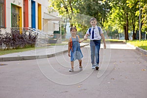 Cheerful schoolchildren, a girl and a boy in a white shirt with backpacks, go from school.