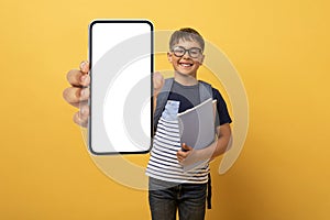 Cheerful schooler boy showing smartphone with empty screen