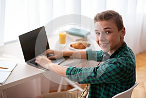 Cheerful schooler having break from studying, typing on laptop