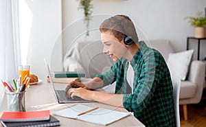 Cheerful schooler with headset typing on laptop