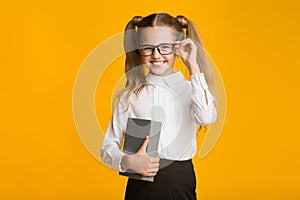 Cheerful Schoolgirl In Eyeglasses Posing With Book On Yellow Background