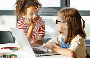 Cheerful schoolgirls doing a school assignment using a laptop during online lesson