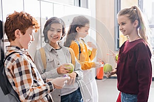 Cheerful schoolkids with apples talking near