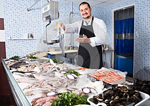 Cheerful seller in black apron showing fish photo