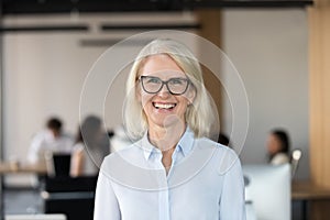 Cheerful senior businesswoman in glasses looking at camera in office