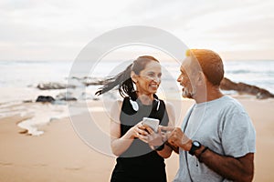 Cheerful senior caucasian lady and man in sportswear use phone app, enjoy training and active lifestyle on beach