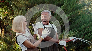 Cheerful Senior Couple Having Fun In Garden, Playing With Water Hose Outdoors