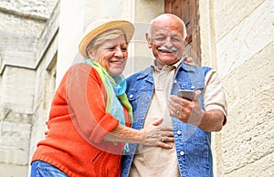 Cheerful senior couple having fun with new smart phone social trends - Happy old people using mobile device outdoor - Concept of