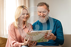 Cheerful Senior Couple Holding Paper Travel Map, Planing Vacation Indoor