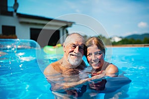 Cheerful senior couple in swimming pool outdoors in backyard, looking at camera.
