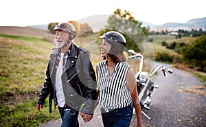 A cheerful senior couple travellers with motorbike in countryside.