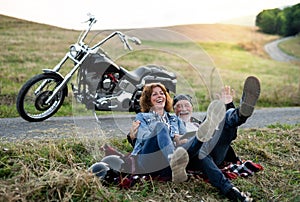 A cheerful senior couple travellers with motorbike in countryside.