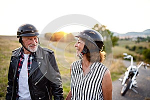 A cheerful senior couple travellers with motorbike in countryside.