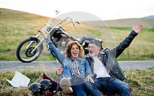 A cheerful senior couple travellers with motorbike in countryside.