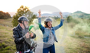 A cheerful senior couple travellers with motorbike in countryside, having fun.