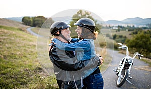 A cheerful senior couple travellers with motorbike in countryside, hugging.
