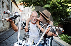 A cheerful senior couple travellers with motorbike in town.