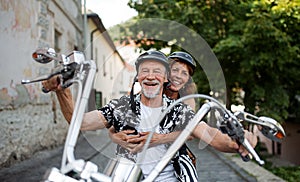 A cheerful senior couple travellers with motorbike in town.